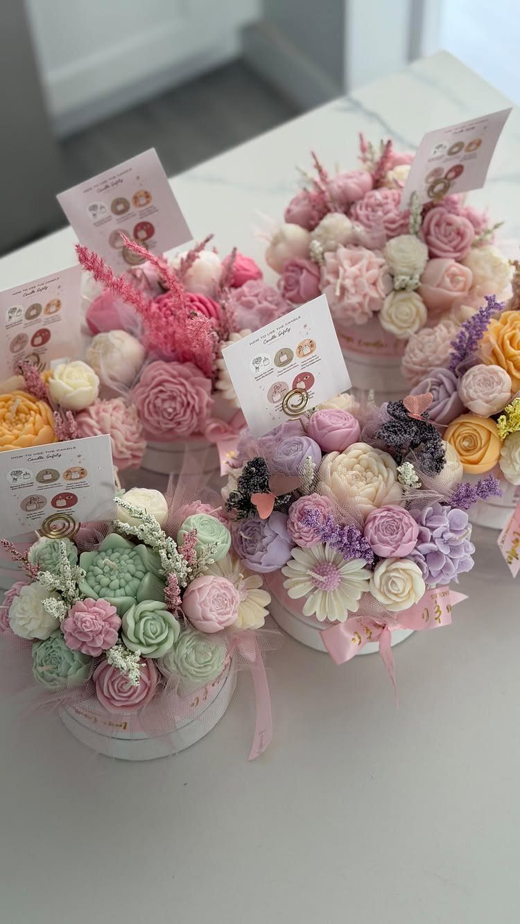 Pastel wax flower arrangements in white round boxes with small gift tags.