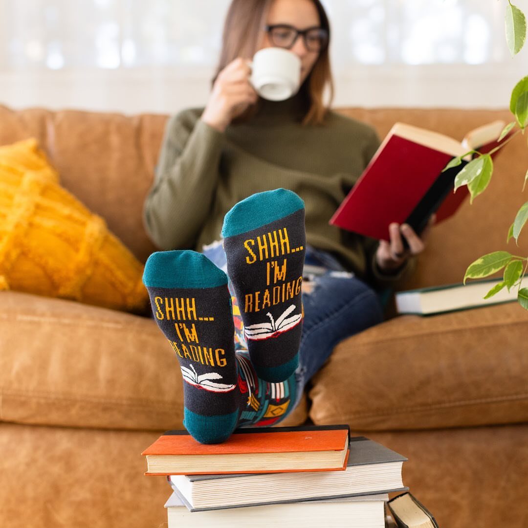 Blue reading-themed socks resting on a stack of books on a brown sofa