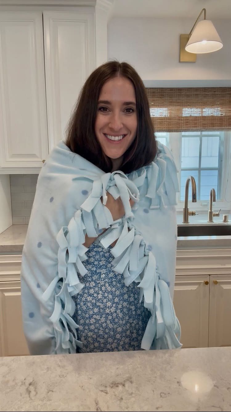 Woman wrapped in a light blue tied fleece blanket in a white kitchen