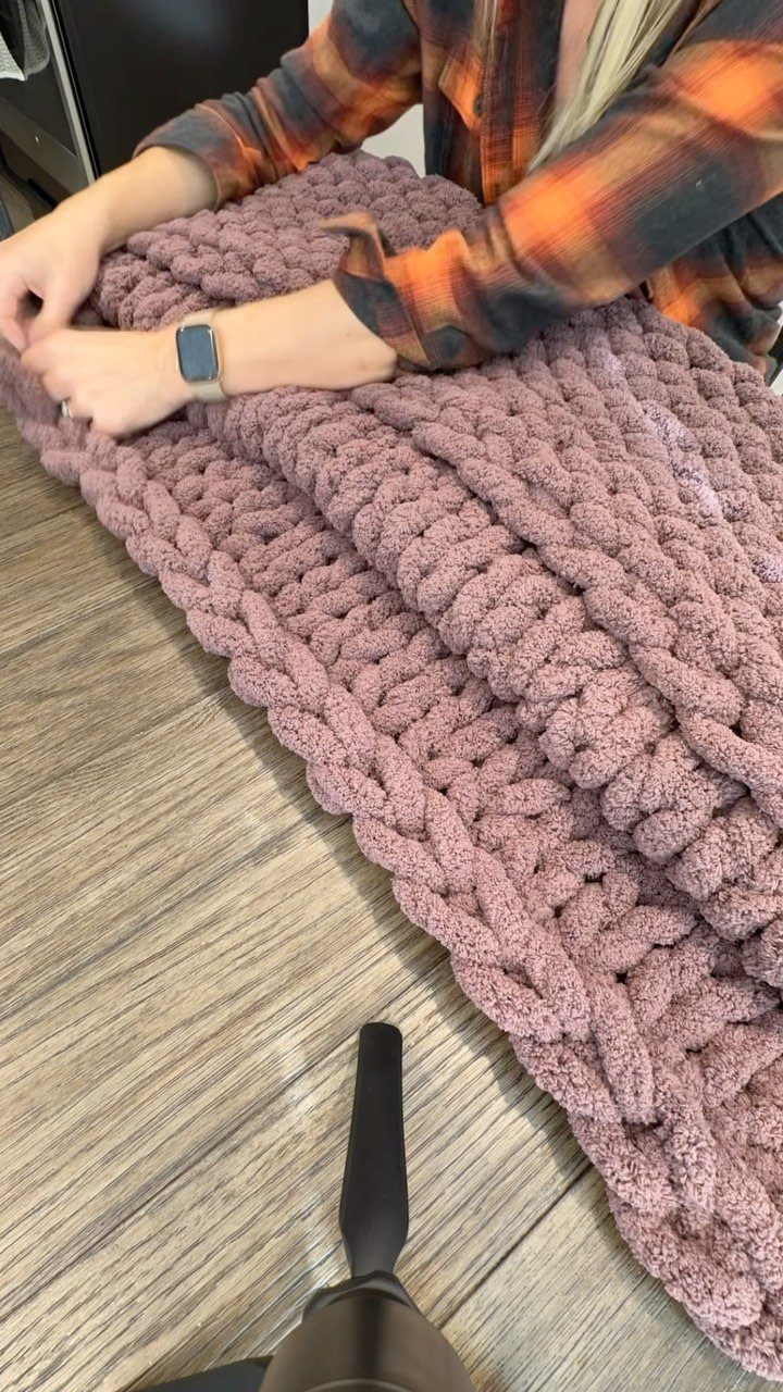 Dusty rose chunky knit blanket draped over a person's lap on wood flooring