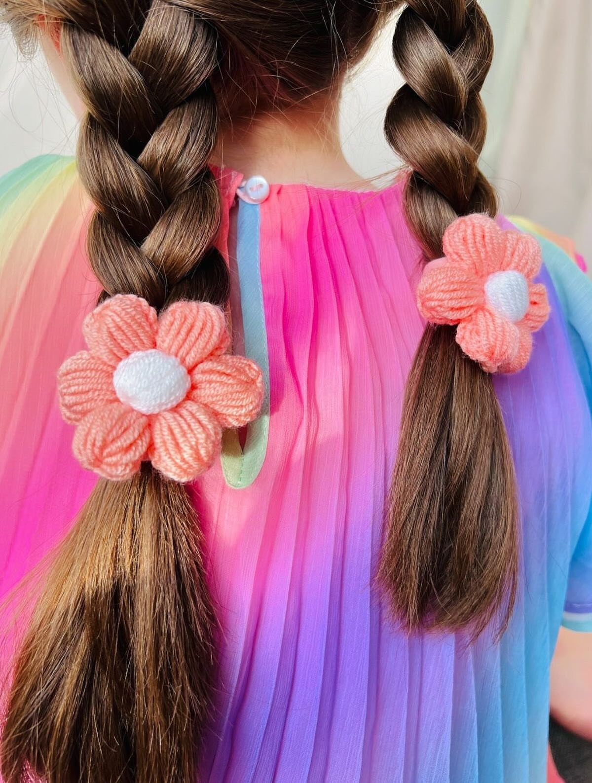Two brown braids secured with peach crocheted flower hair ties on rainbow clothing