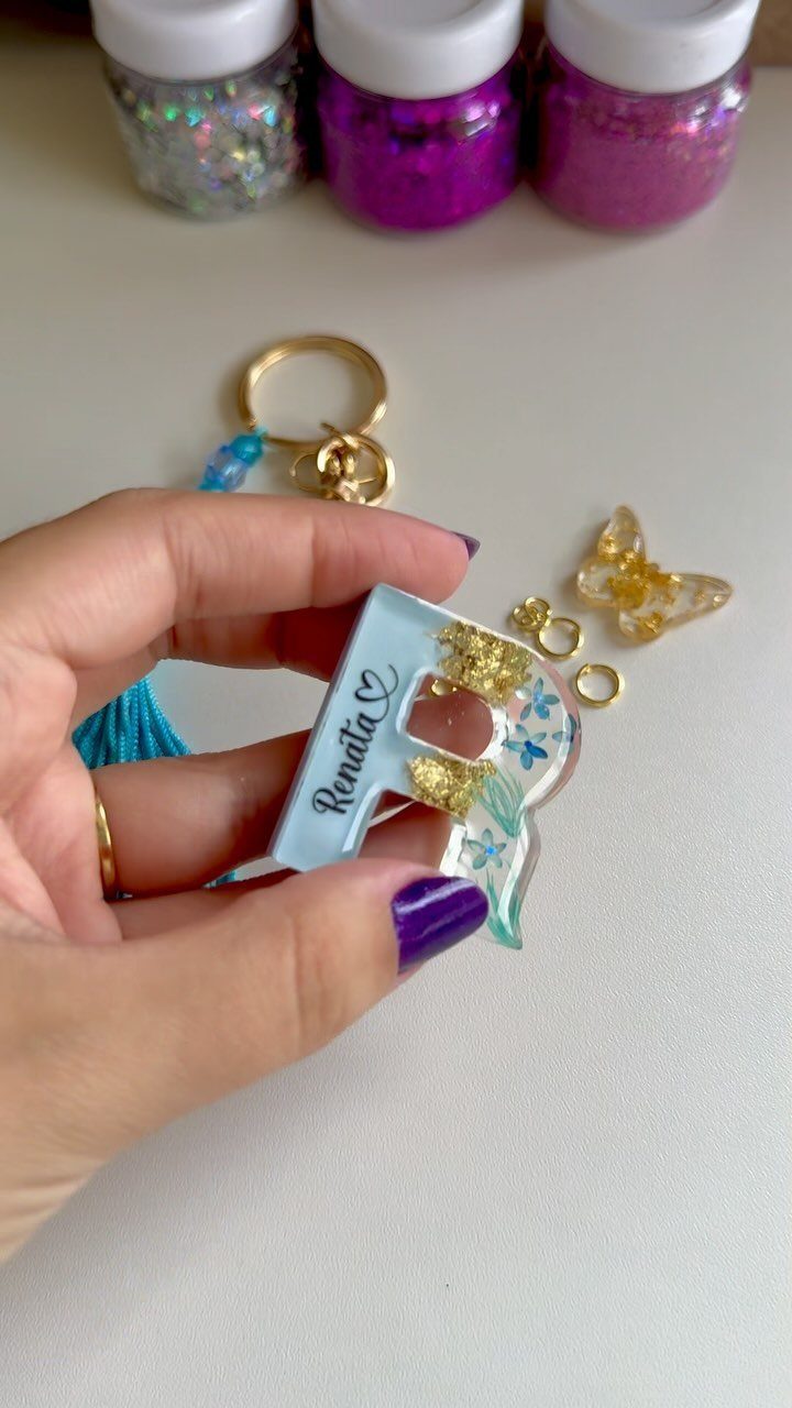 Light blue resin letter R keychain with gold flakes held by a hand.