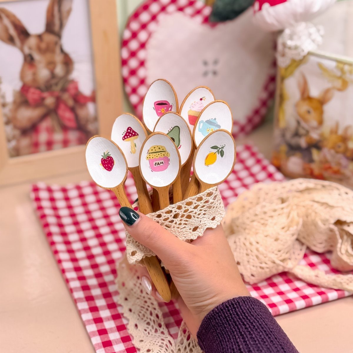 Wooden spoons decorated with colorful decoupage images held by a hand over lace.
