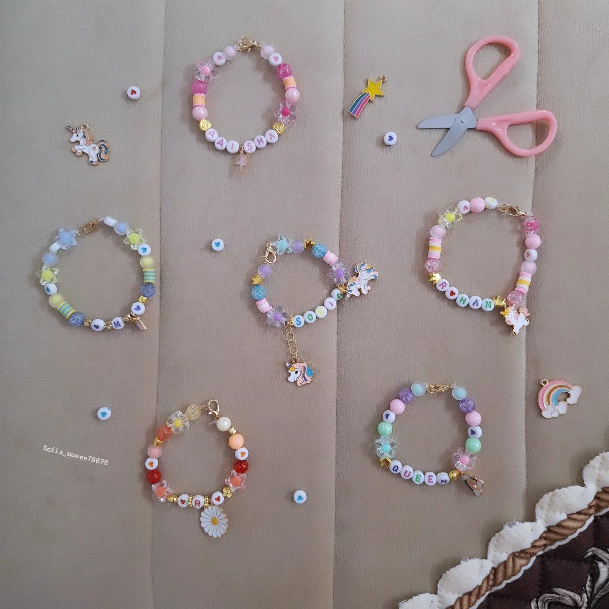 Colorful beaded friendship bracelets with letter beads and charms on beige fabric.