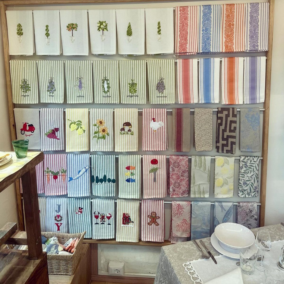 Embroidered tea towels with colorful designs displayed on a wooden wall rack.