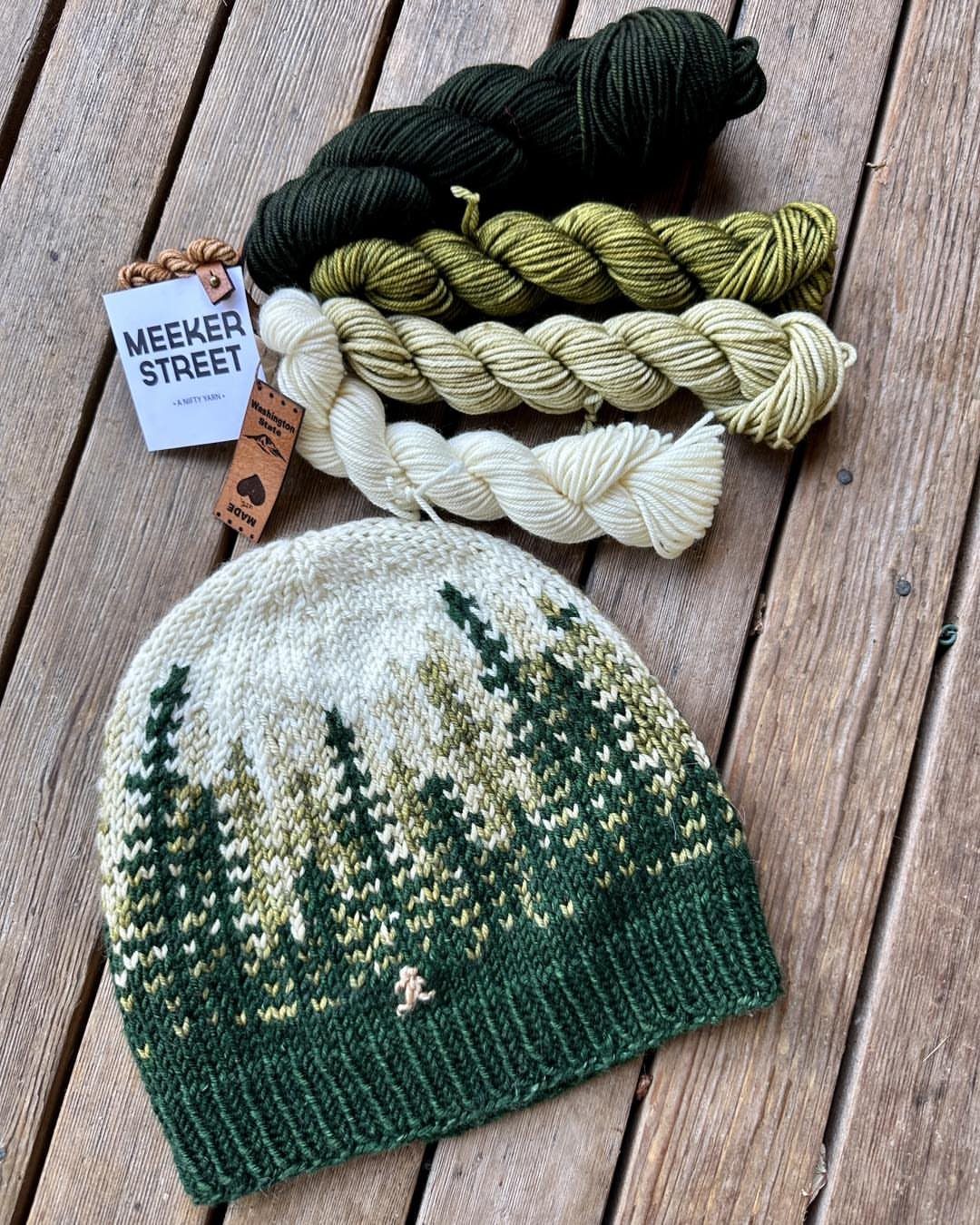 Knitted beanie with forest pattern and matching yarn hanks on wooden deck