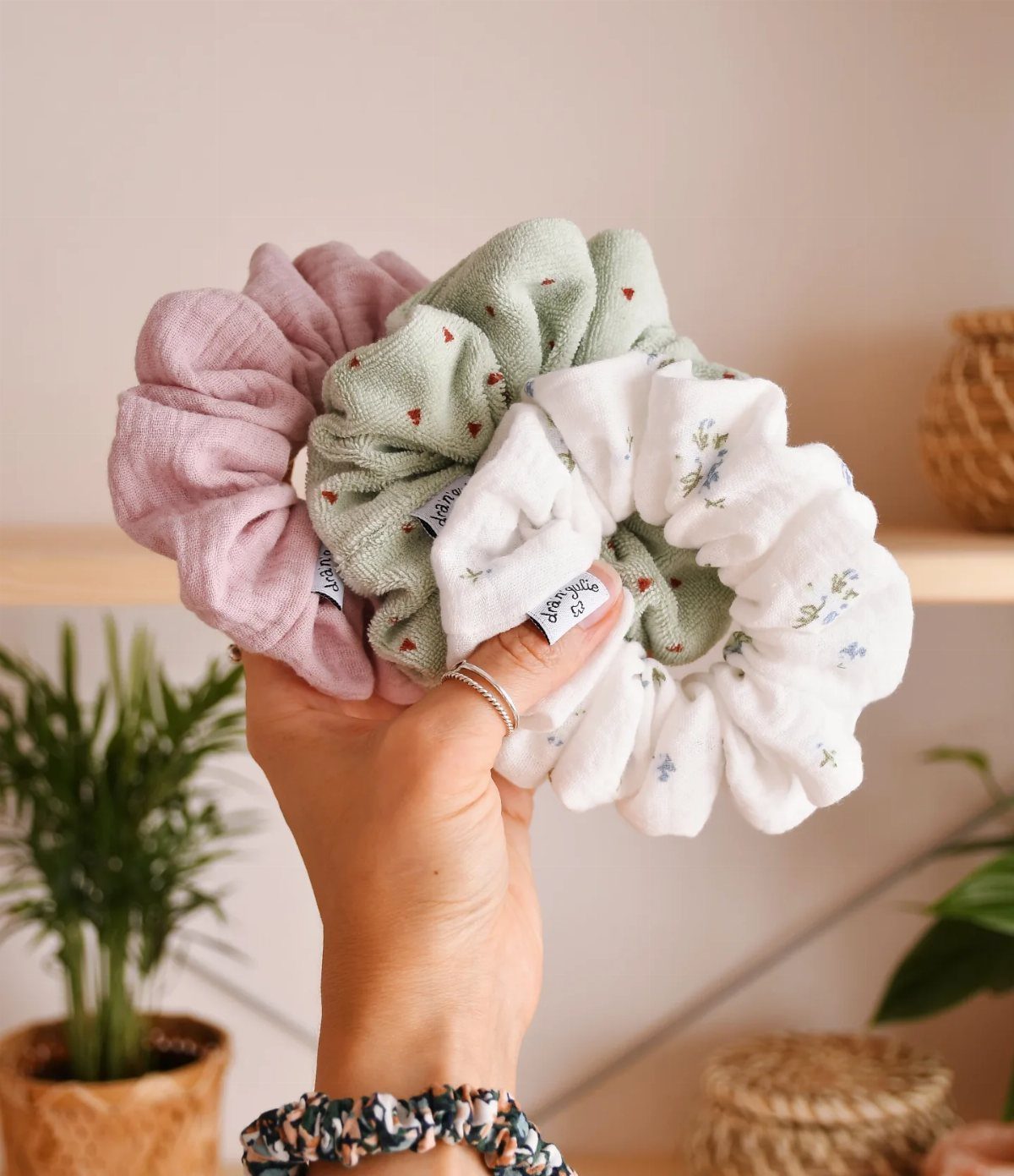 Three fabric hair scrunchies in pink, green, and white held in a hand.