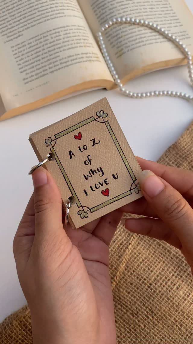Handmade small brown paper booklet with love notes held by two hands.