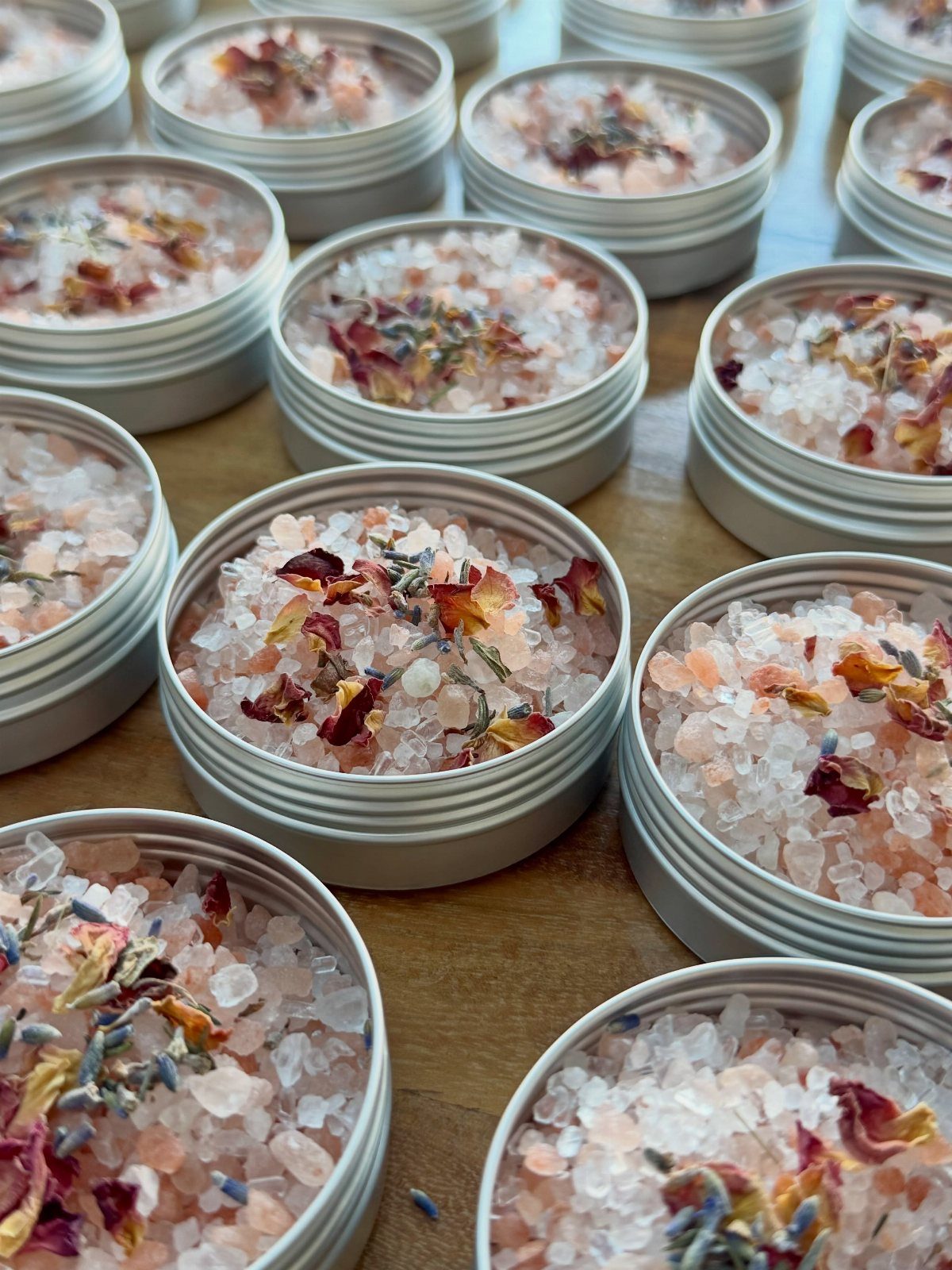 Silver metal tins filled with pink bath salts and dried flower petals.