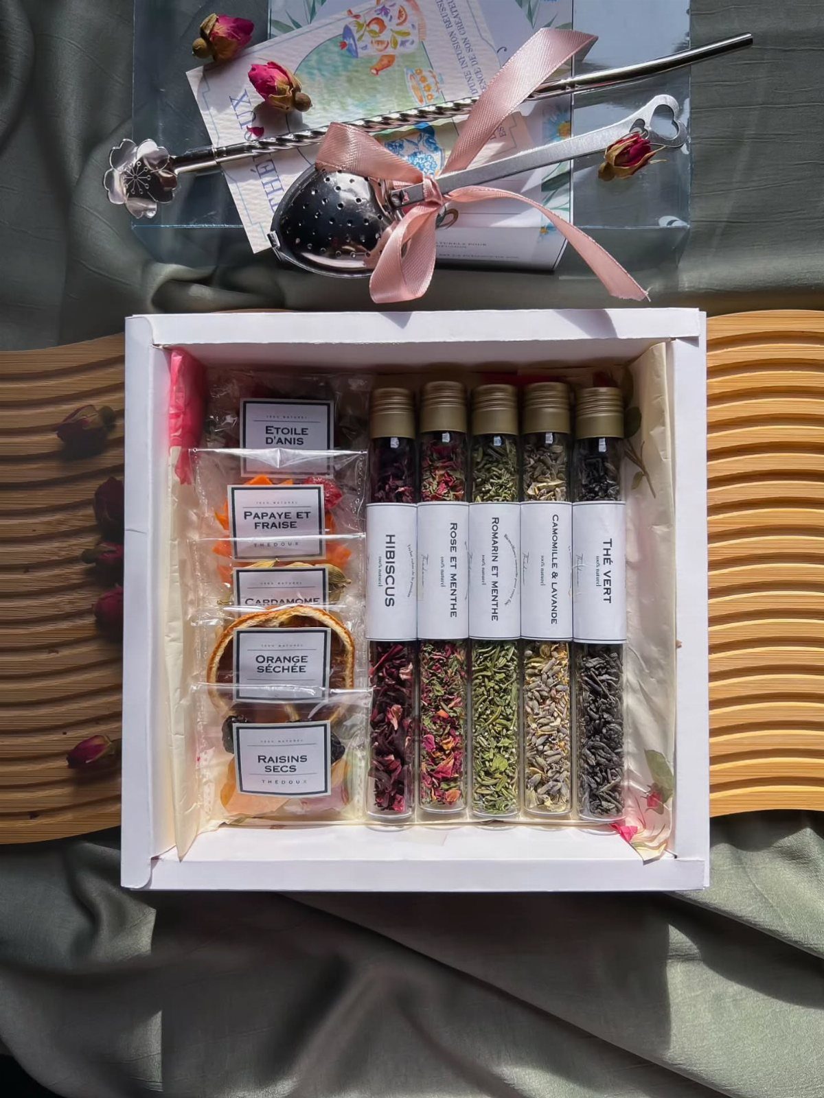 Assorted dried tea blends in glass tubes and packets inside a white gift box.