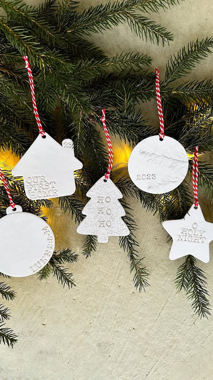 White clay ornaments with imprinted text hanging on green pine branches with lights.