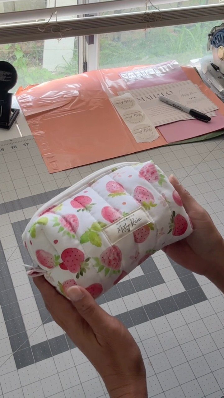 Strawberry print quilted zipper pouch held by hands over a grey cutting mat