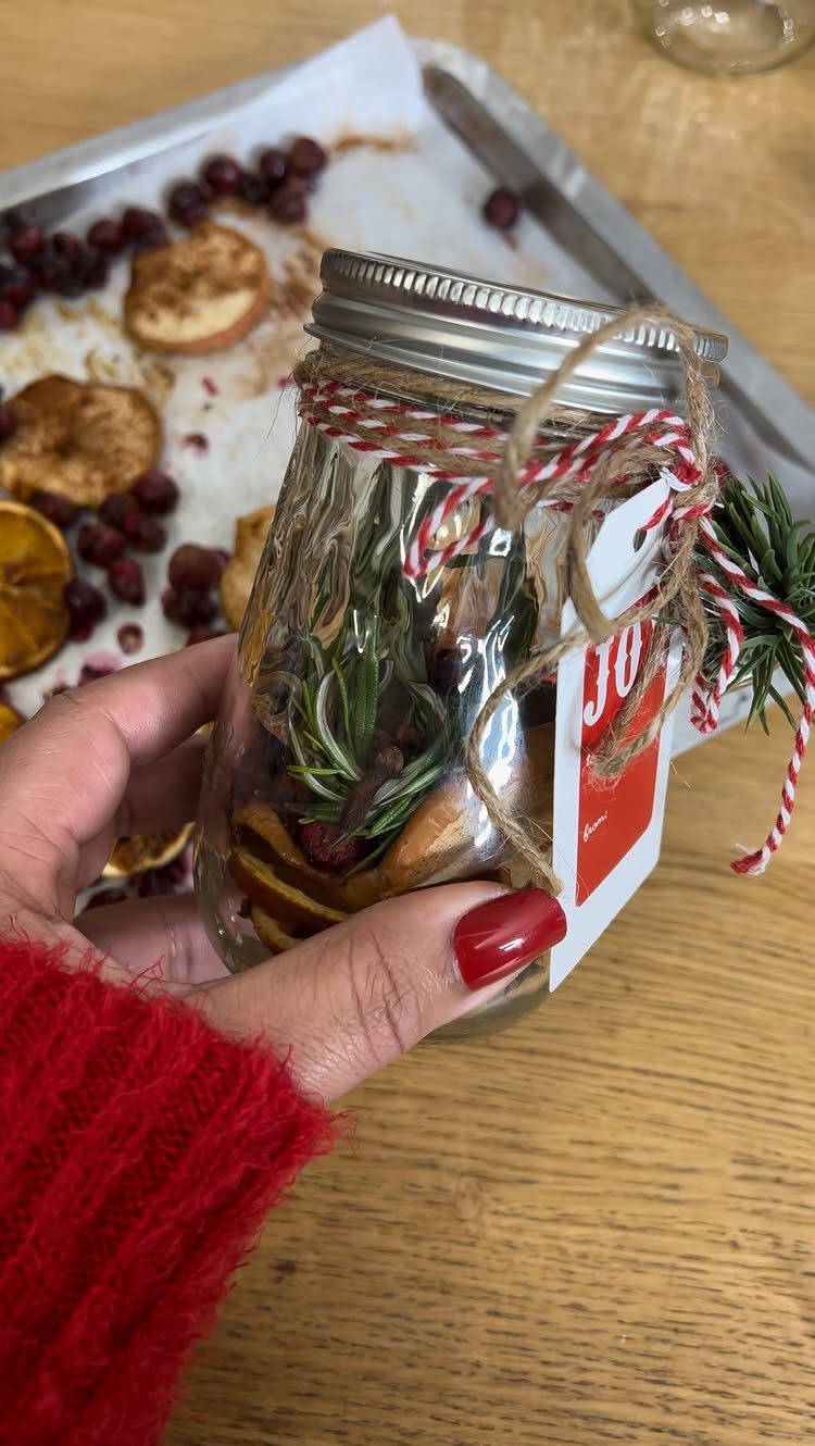 Glass jar filled with dried citrus and herbs tied with festive red twine.