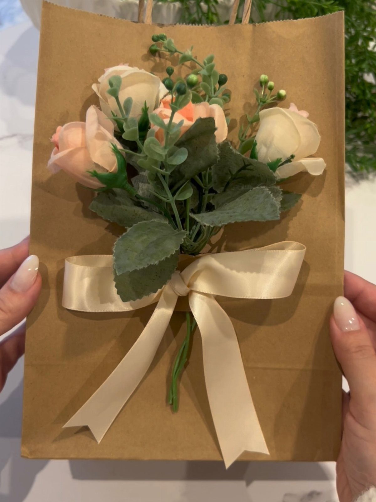 Brown kraft paper bag holding a bouquet of peach roses tied with ribbon.
