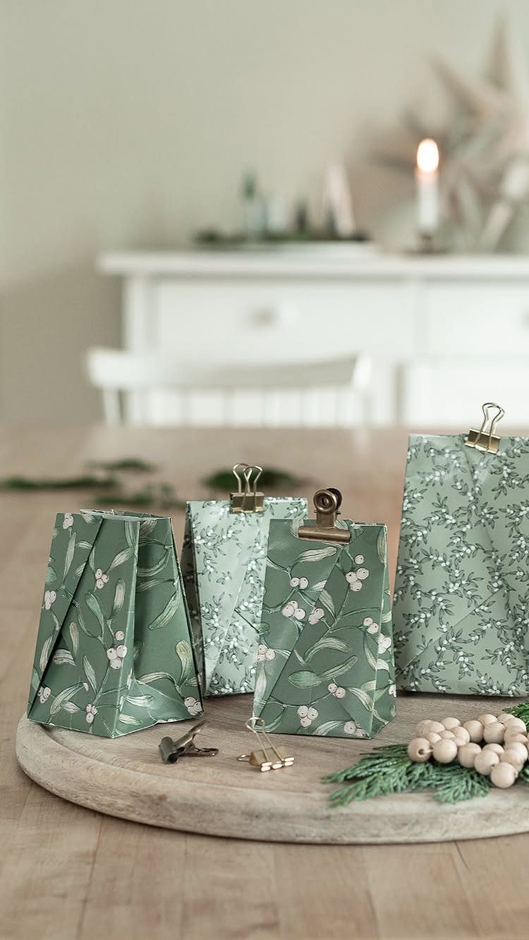 Green floral patterned gift bags with metal clips on a wooden board.