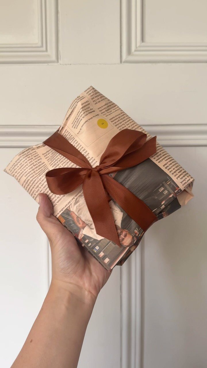 Gift wrapped in newspaper tied with a brown satin ribbon held by a hand