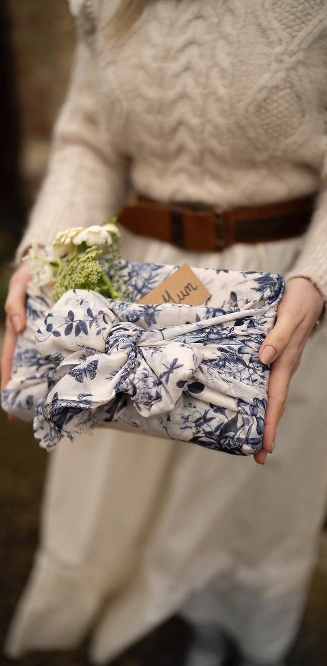 Gift wrapped in blue and white floral fabric tied with a knot and flowers.