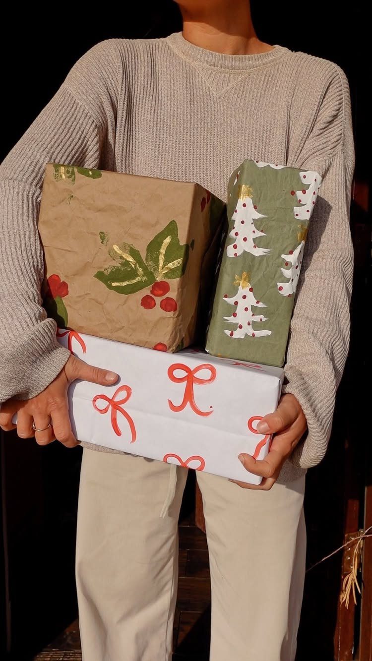 Person holding three gifts wrapped in eco-friendly brown, green, and white paper.