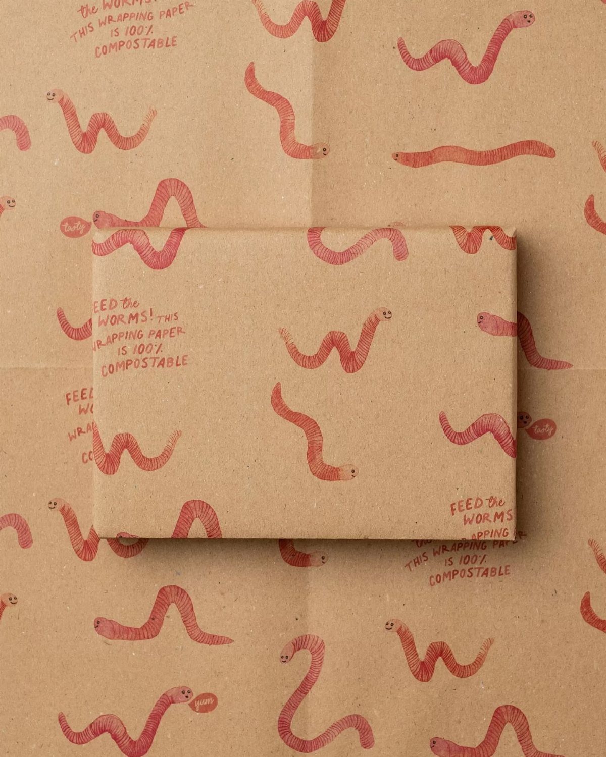 Brown compostable wrapping paper with red worm patterns wrapping a rectangular gift box.