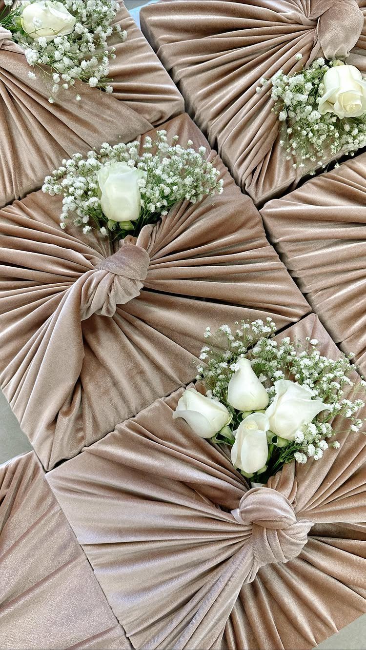 Beige velvet fabric wrapped gifts decorated with white roses and baby's breath.