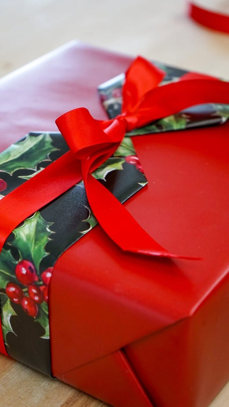 Red wrapped gift with a holly leaf belly band and red satin bow.