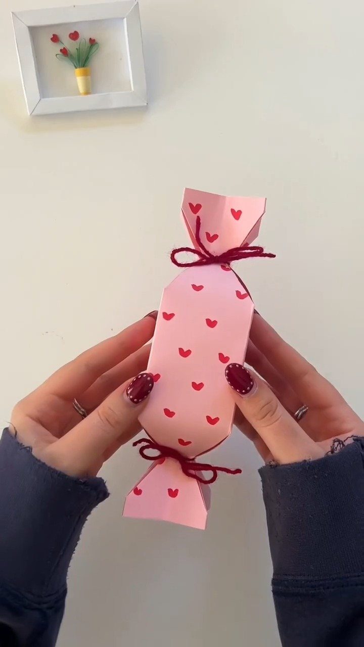 Pink heart-patterned gift wrapped like a candy and held by two hands.