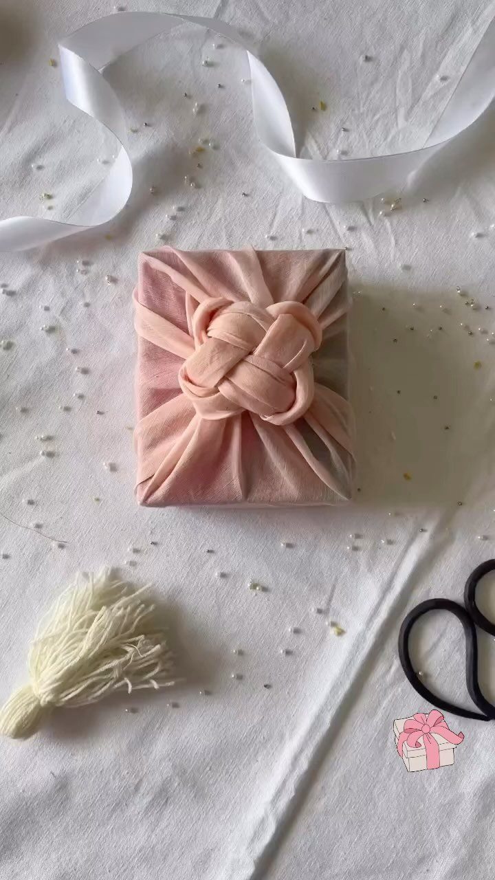 Pink fabric wrapped gift with a decorative knot on white textured cloth