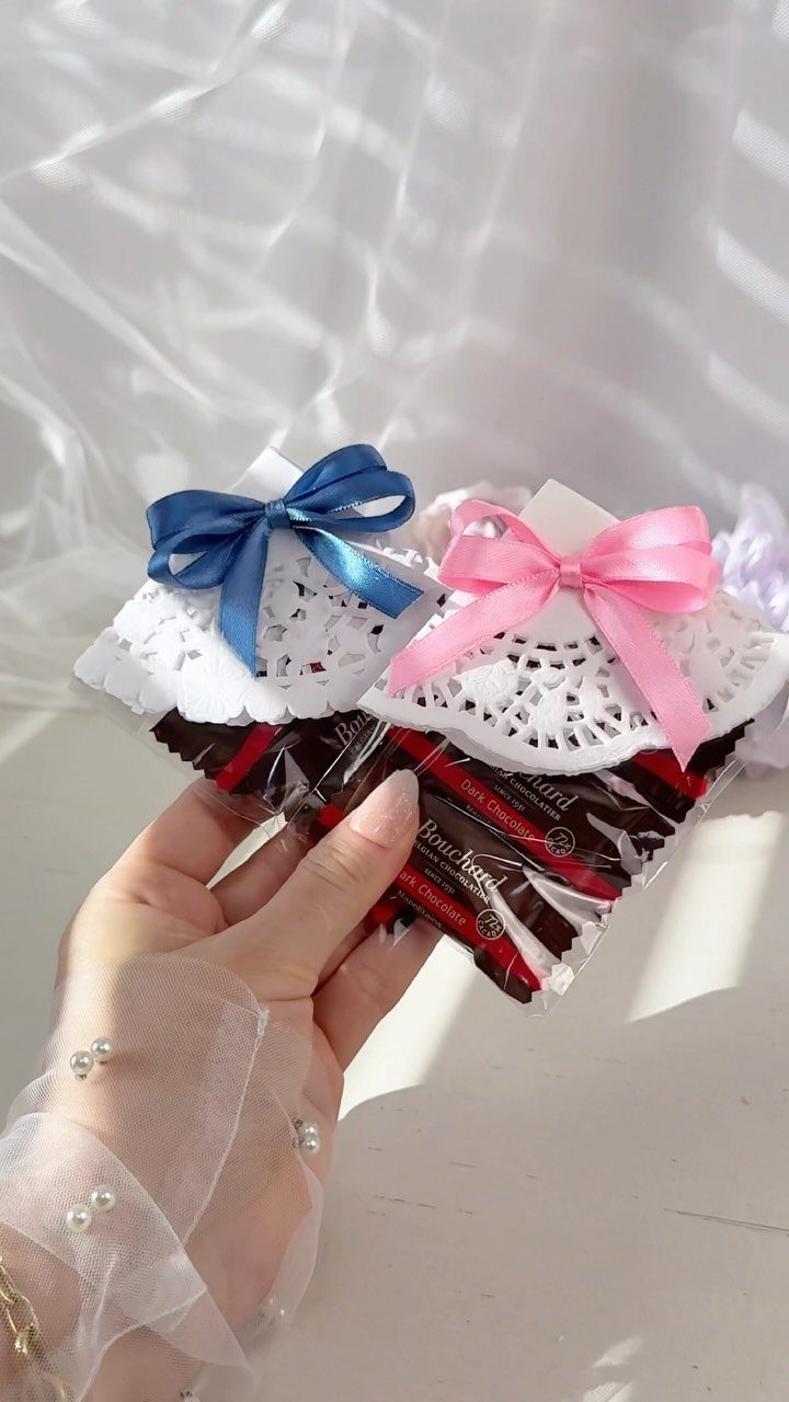 Wrapped chocolate bars with white lace doilies and blue and pink satin bows.