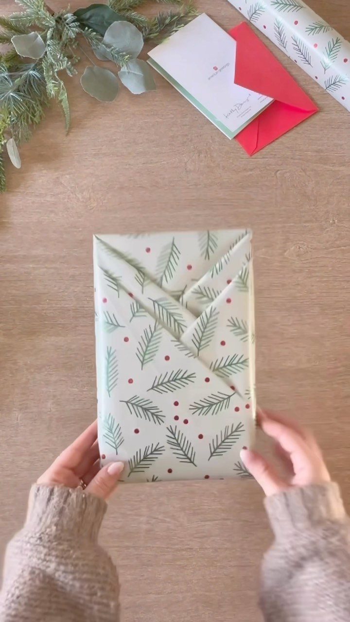 Small gift wrapped in pine needle paper held by hands on wooden table