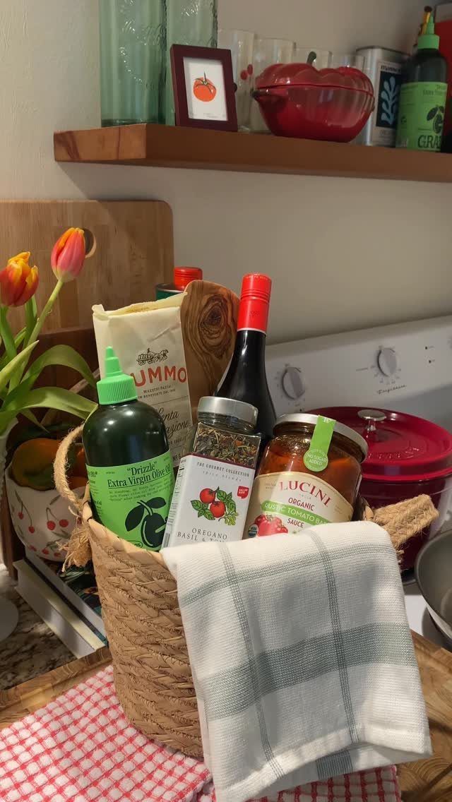 Woven gift basket filled with pasta, sauce, olive oil, and a kitchen towel.