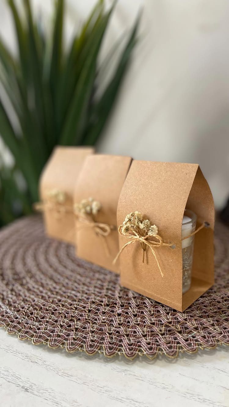Three mini candles in brown kraft paper boxes tied with twine and dried flowers.