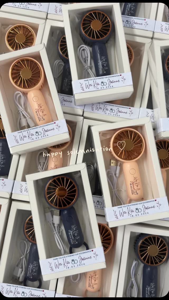 Handheld electric fans in navy and peach colors packaged in white gift boxes.