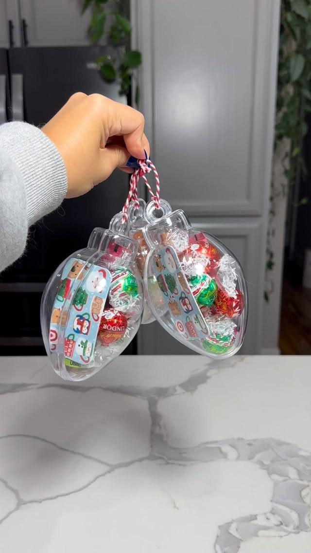 Clear bulb ornaments filled with colorful candies held by a hand over marble.