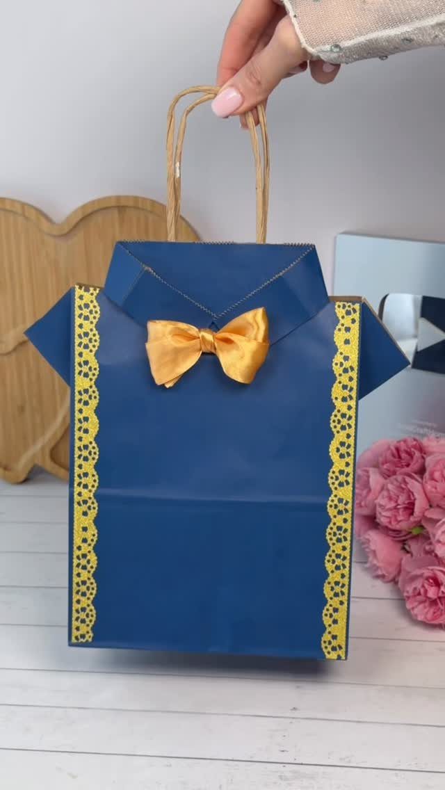 Blue shirt-shaped gift bag with a yellow bow tie held by a hand.