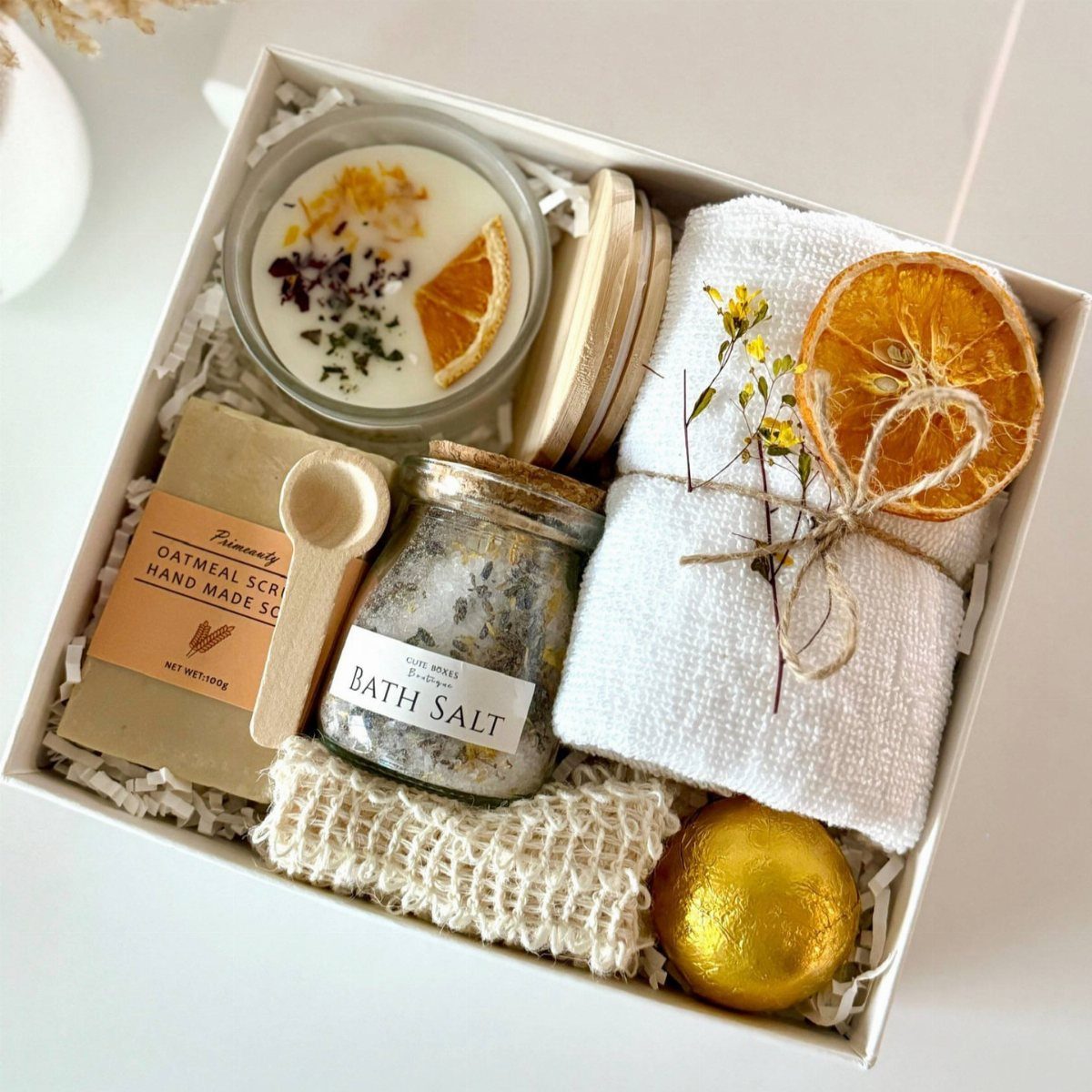 Spa gift box with bath salt, gold bath bomb, candle, and white towel.