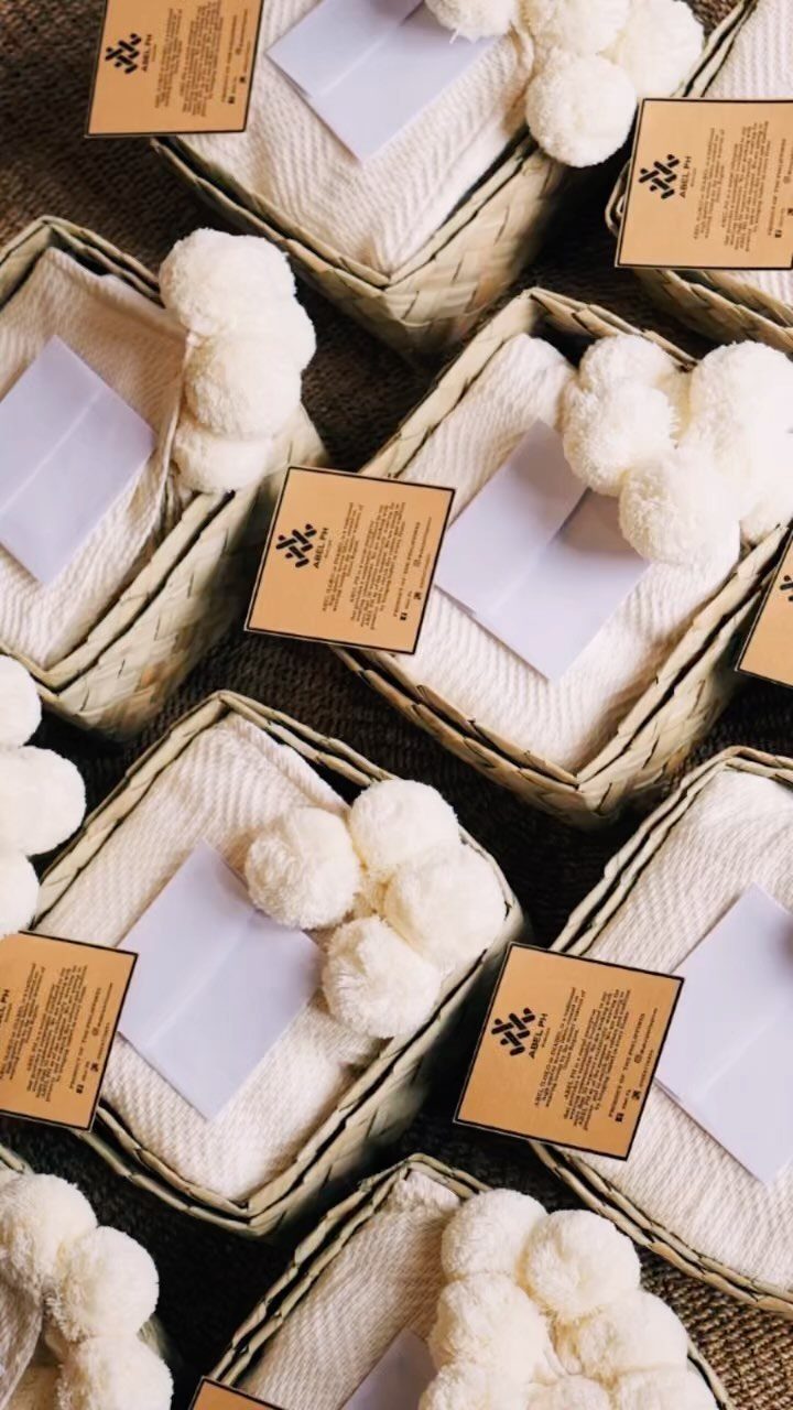 White textured throw blankets with pom-poms in woven baskets with brown gift tags.
