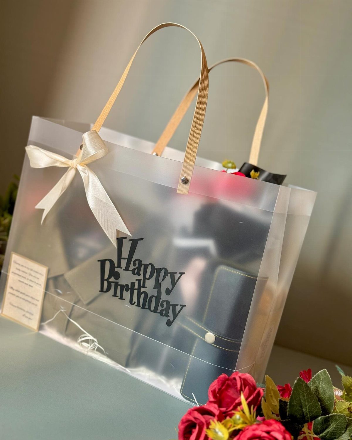 Translucent white birthday gift bag with a white bow and various items inside.