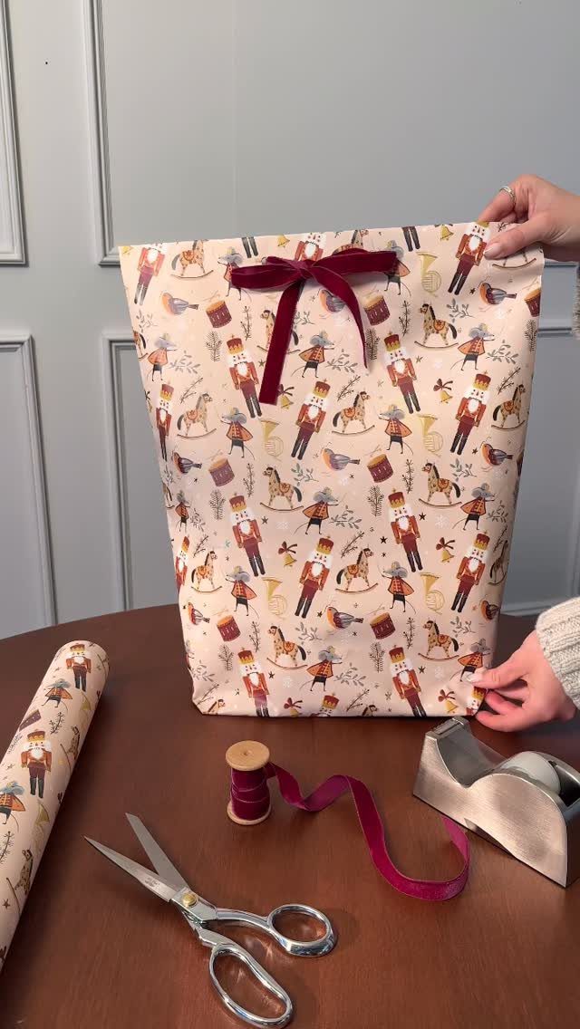 Handmade nutcracker patterned paper gift bag with a red velvet bow and crafting tools.