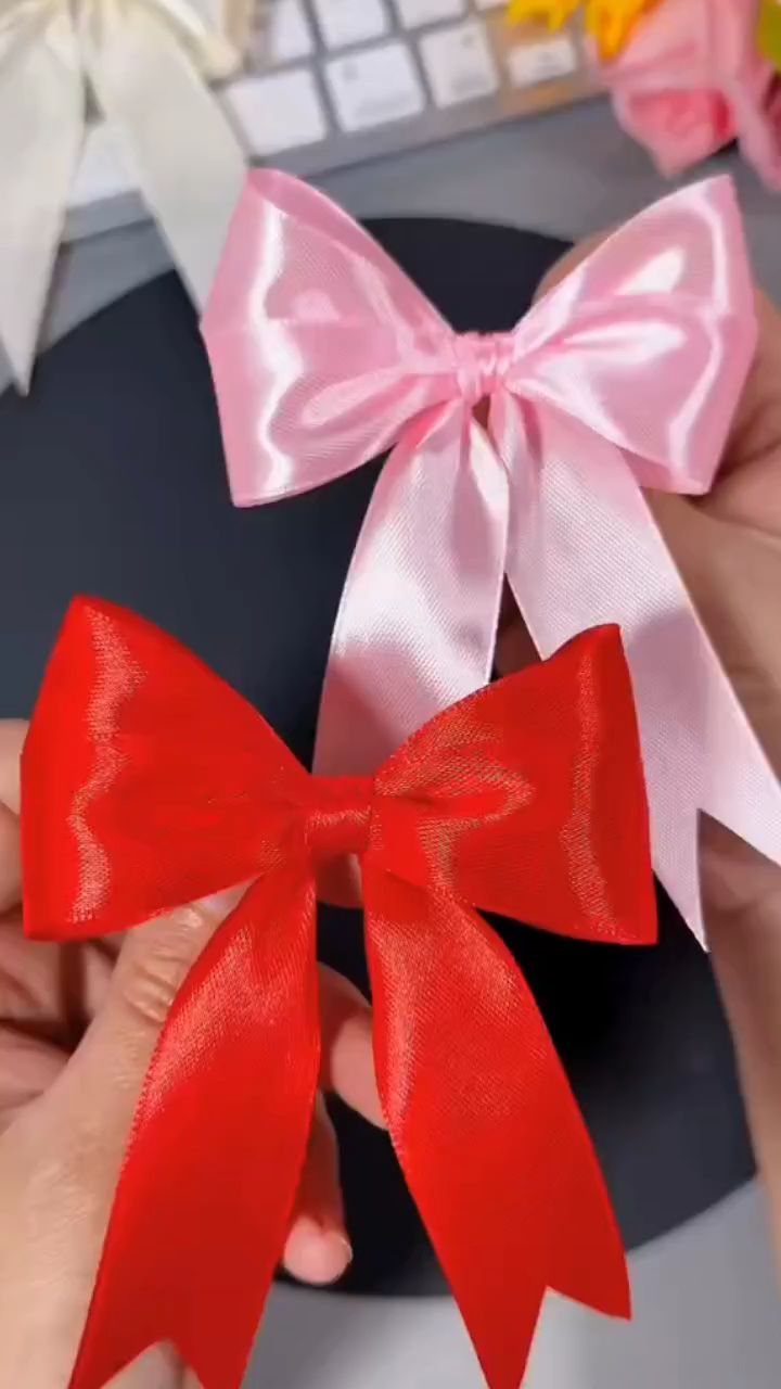 Red and pink satin bows held by hands against a dark background.
