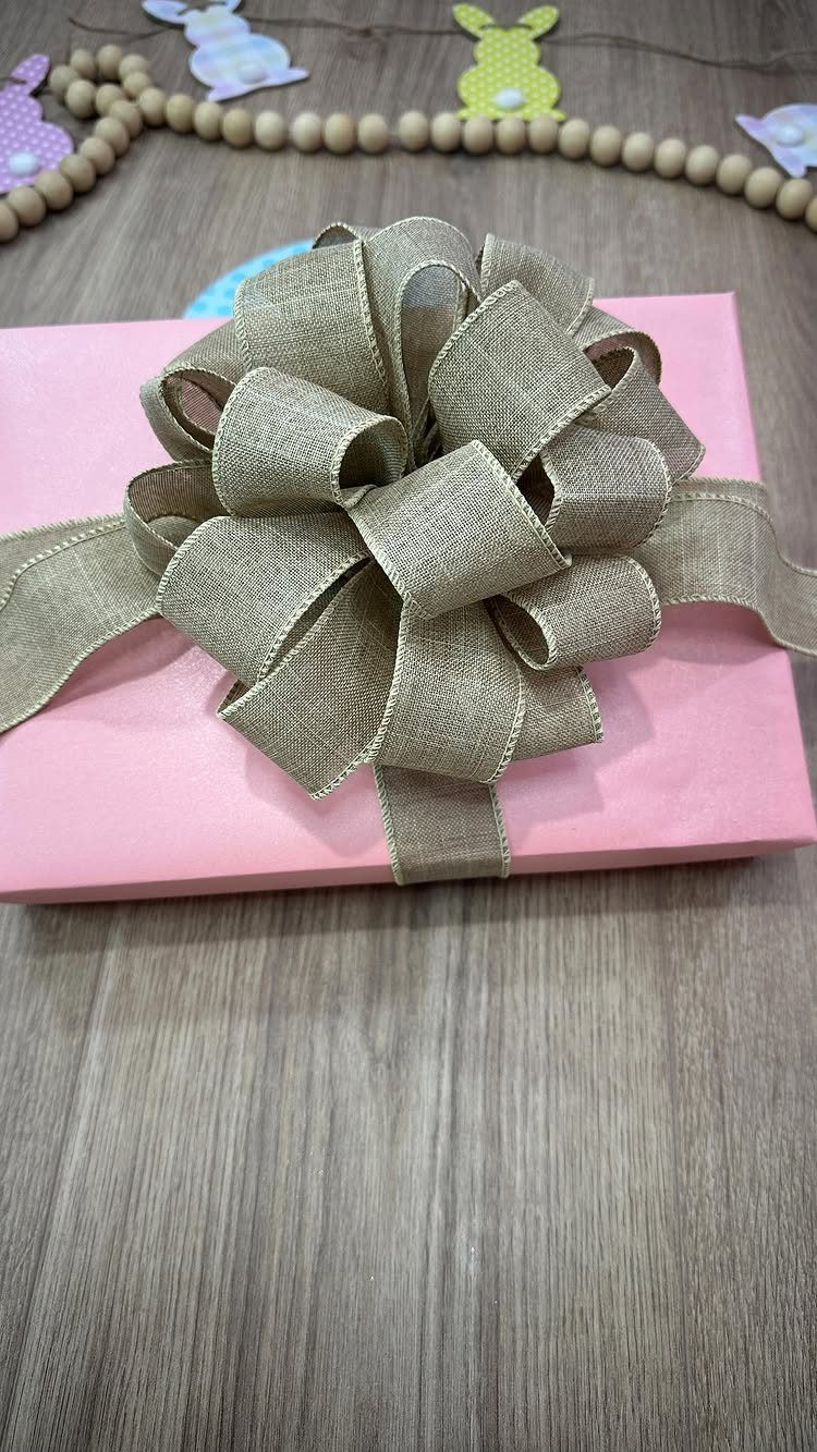 Beige burlap bow tied on a pink gift box over a wooden surface