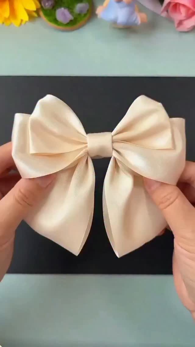 Cream satin bow held by two hands over a black background.