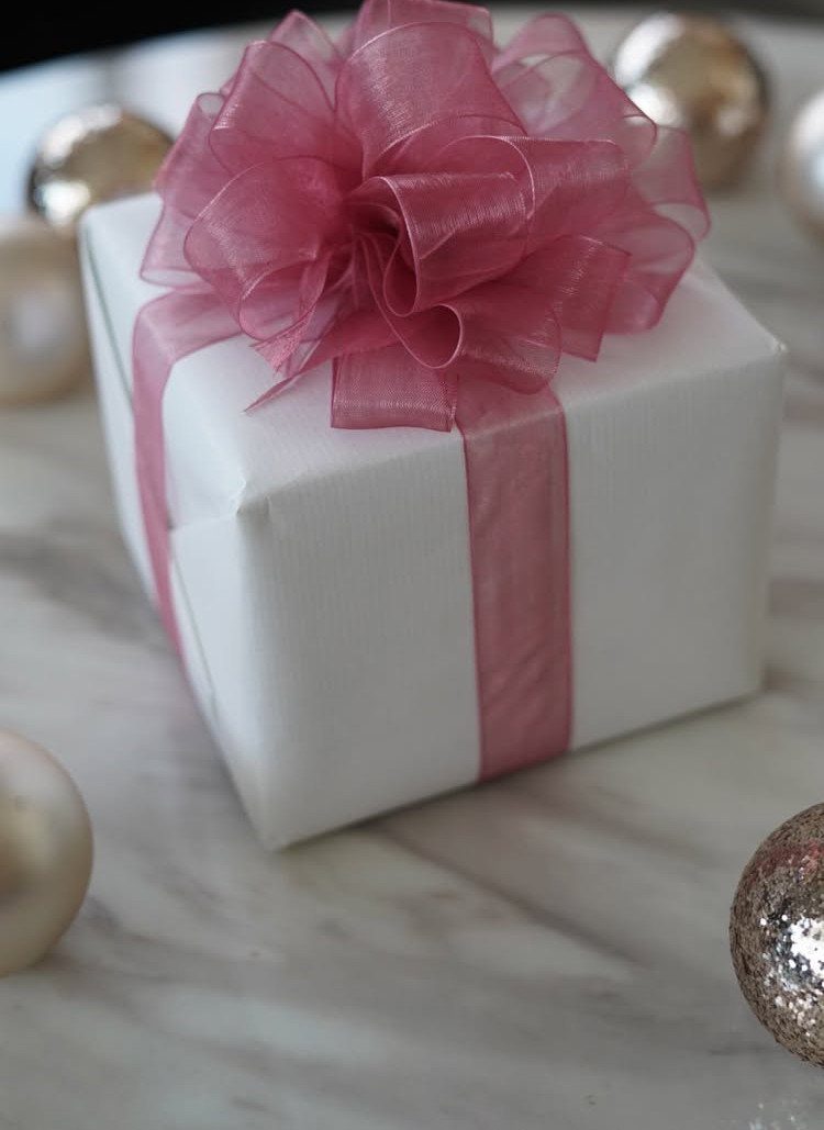 White gift box with a large, layered pink organza bow on marble surface