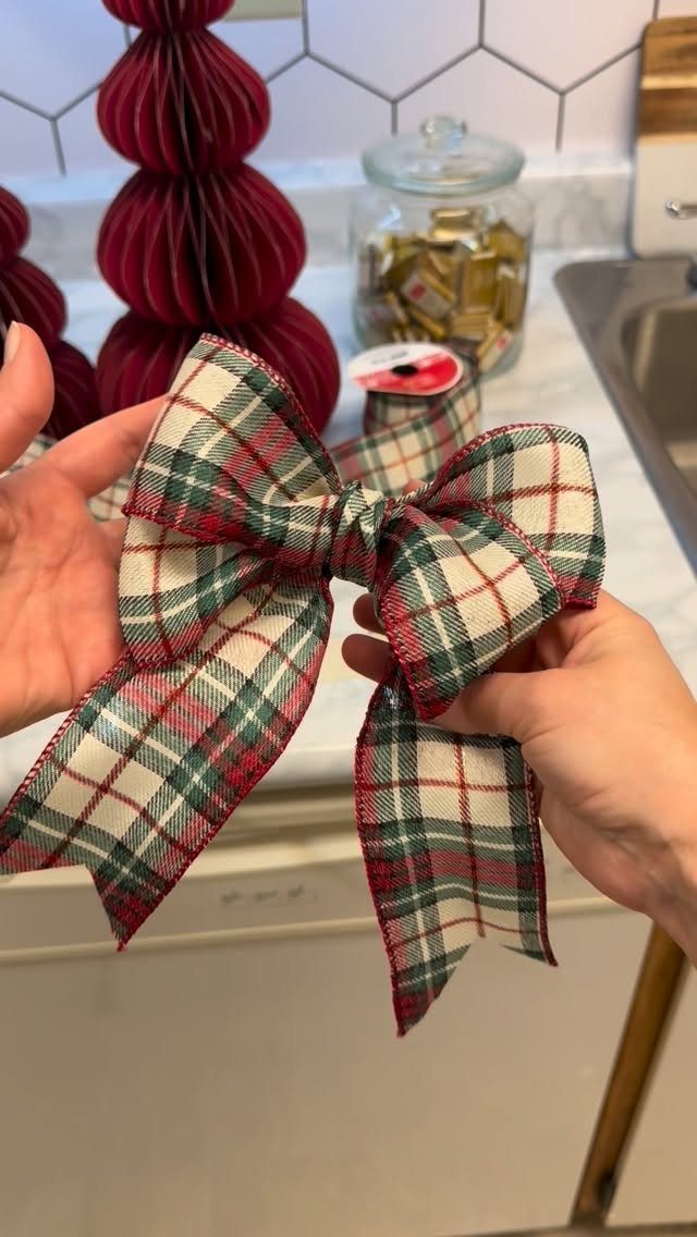 Hands holding a finished red and green plaid fabric gift bow in a kitchen