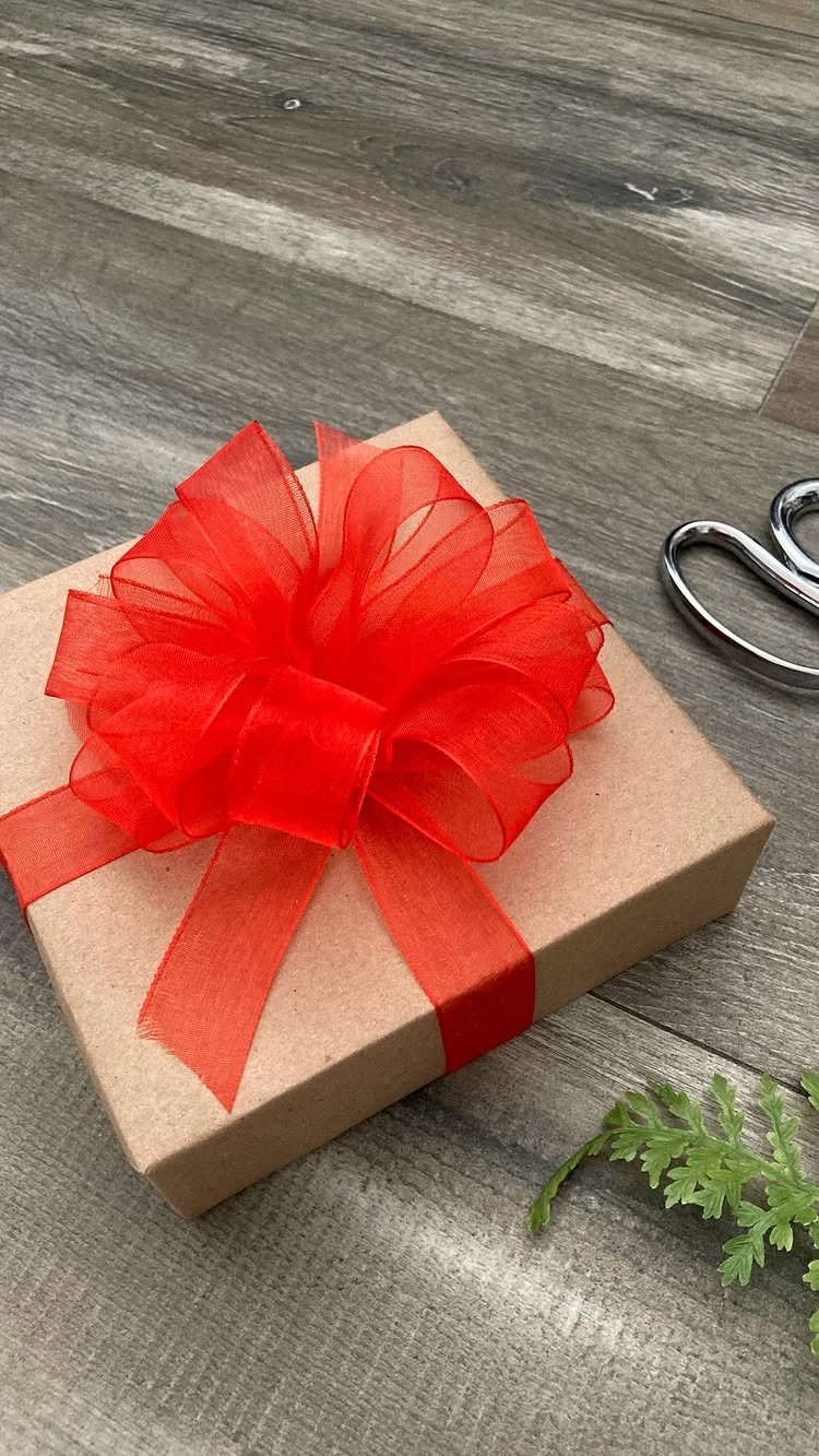 Brown cardboard gift box with a large, fluffy red organza bow on wood.