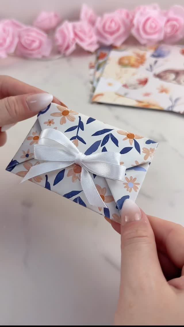 Small floral wrapped gift box with a white satin bow held by hands.