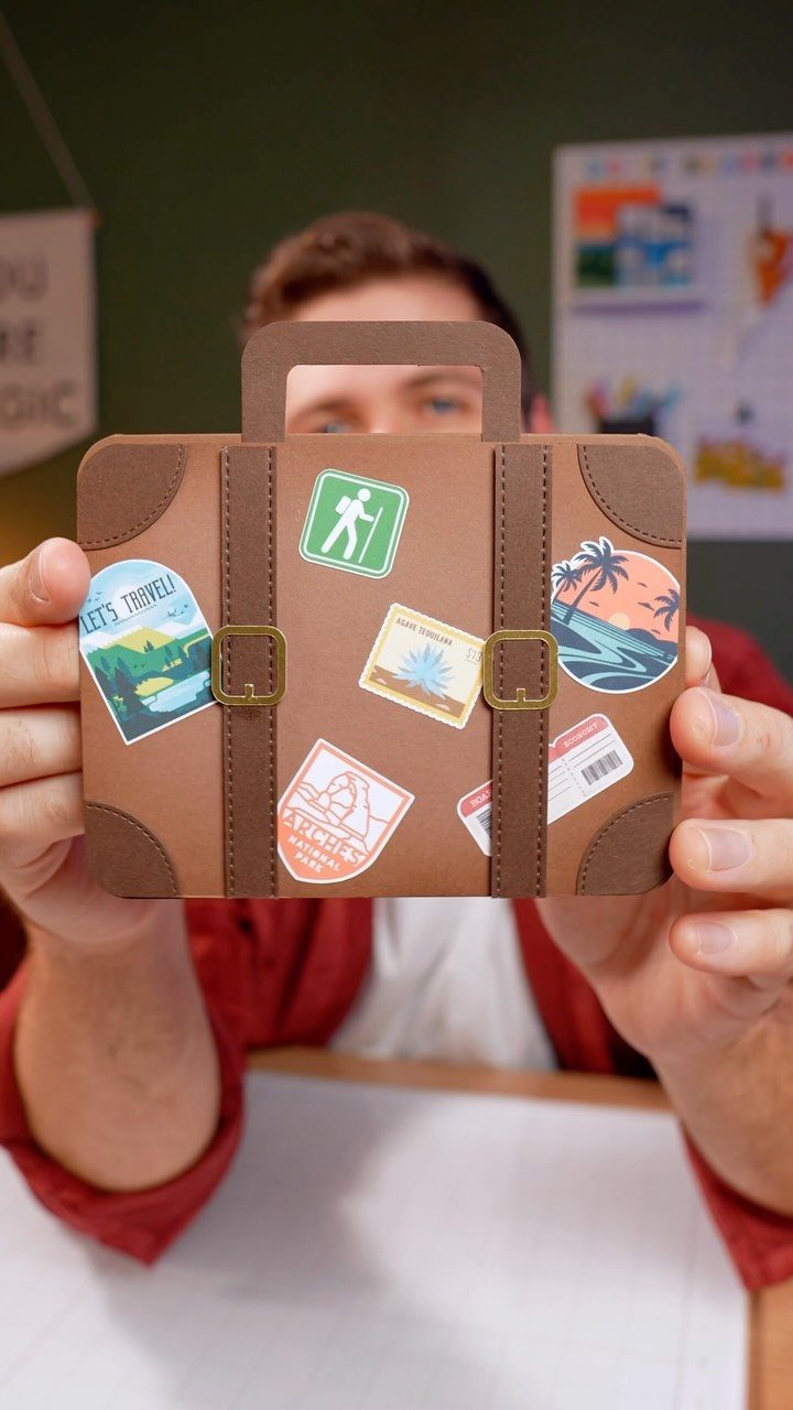 Small brown suitcase-shaped gift box with travel stickers held by a person.