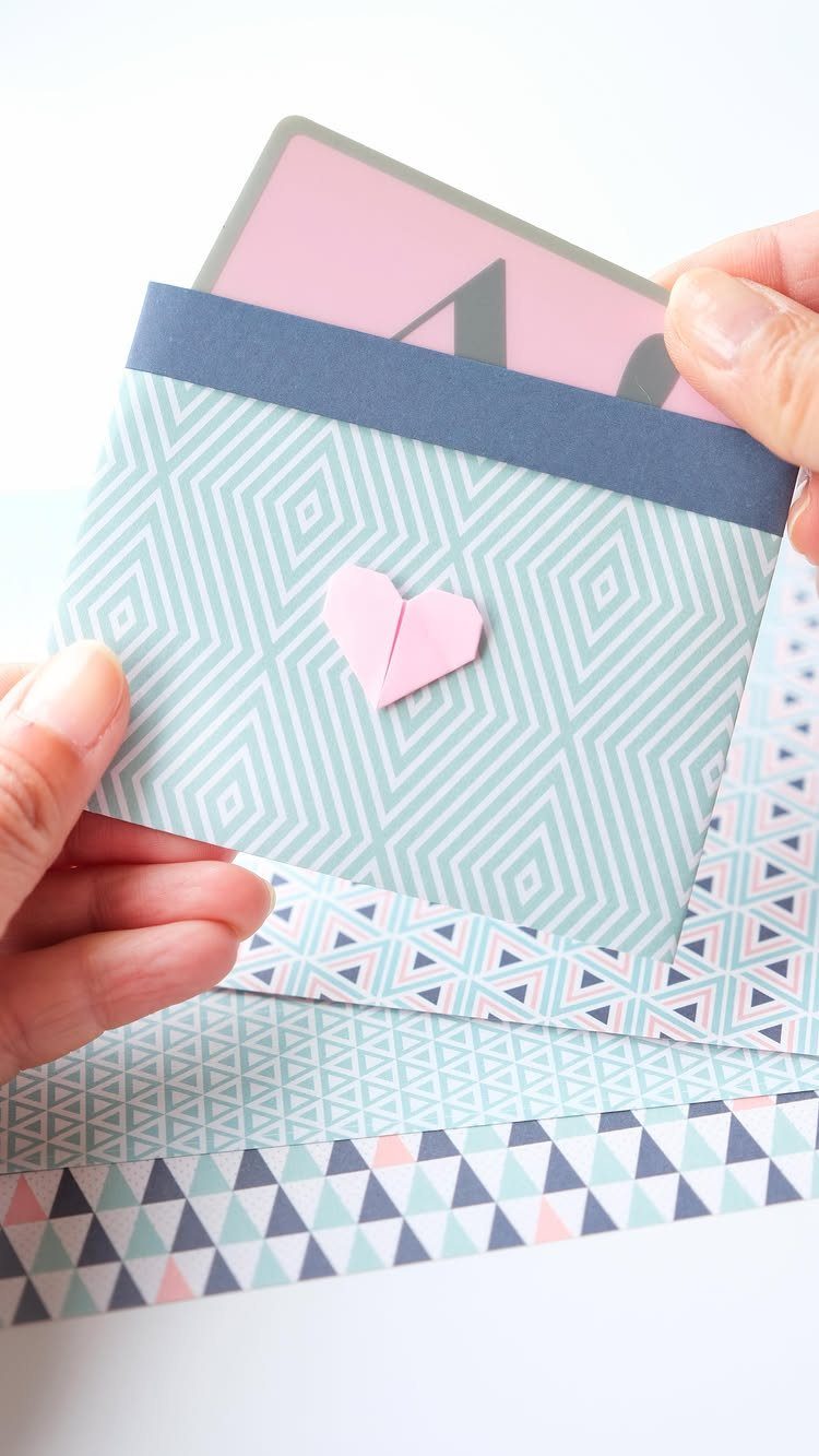 Hands holding a patterned paper envelope with a pink heart seal and gift card.