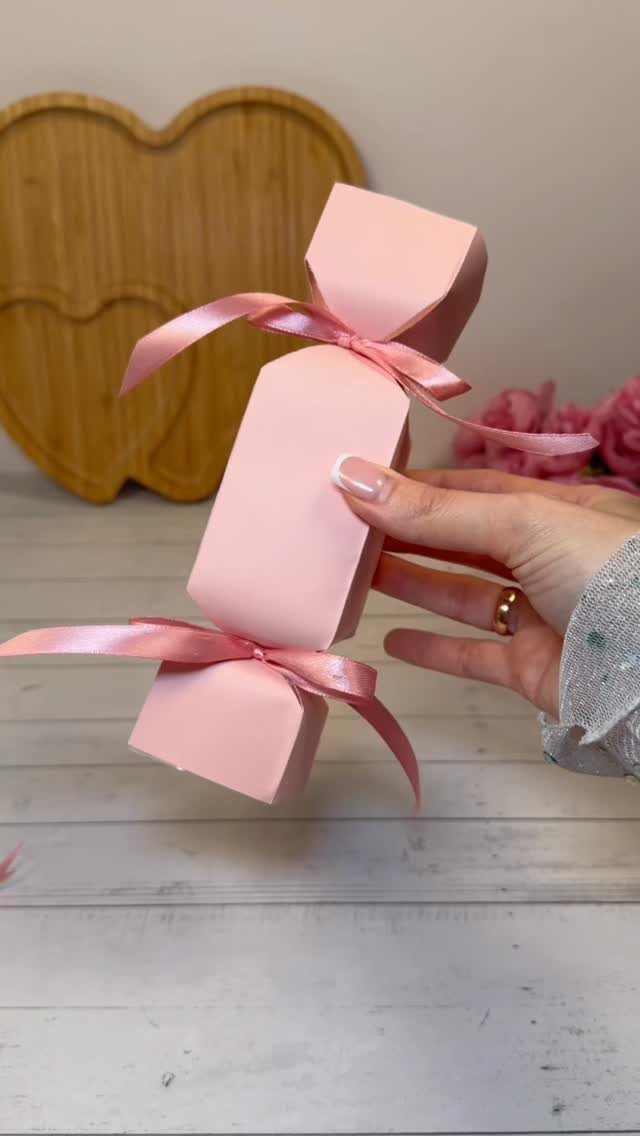 Pink candy-shaped gift box tied with satin ribbons held by a hand.