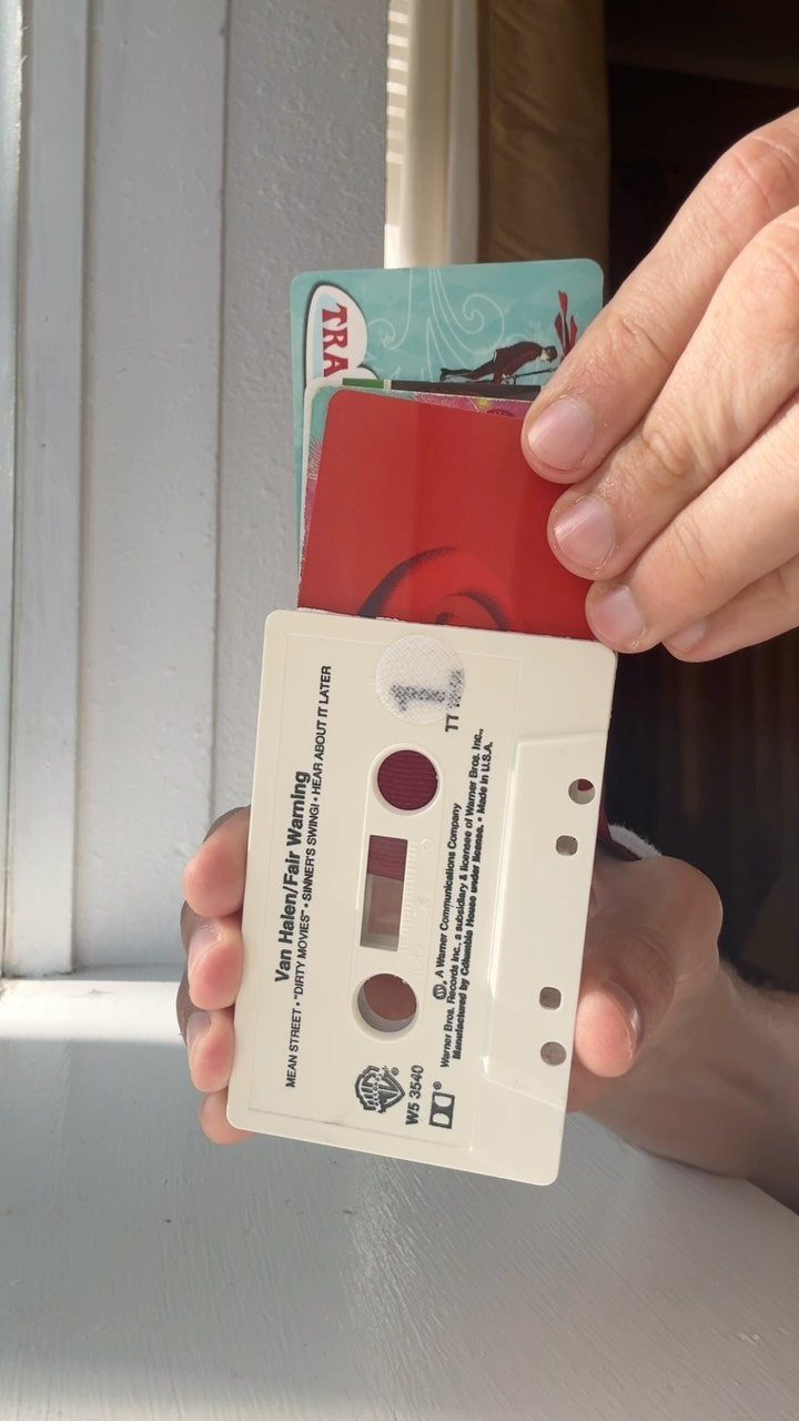 Cassette tape case holding two colorful gift cards held by a person's hands.