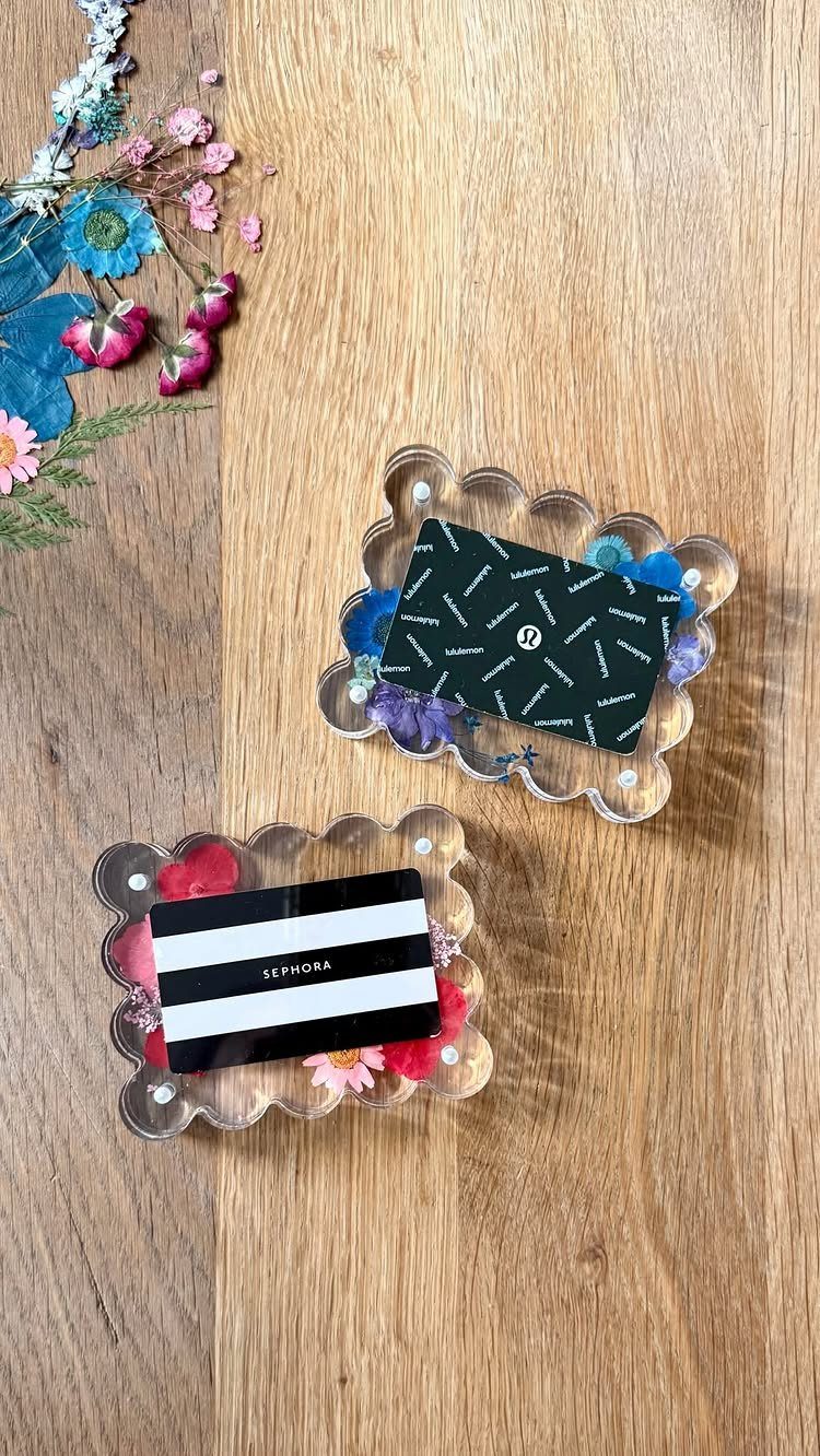 Gift cards presented in clear scalloped trays with colorful dried flowers on wood.